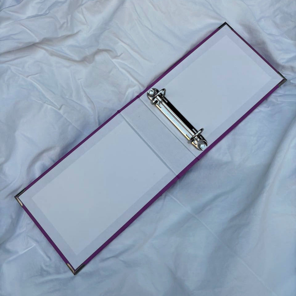 Open folder for nail art stamping plates with a metal clip inside on a white fabric background