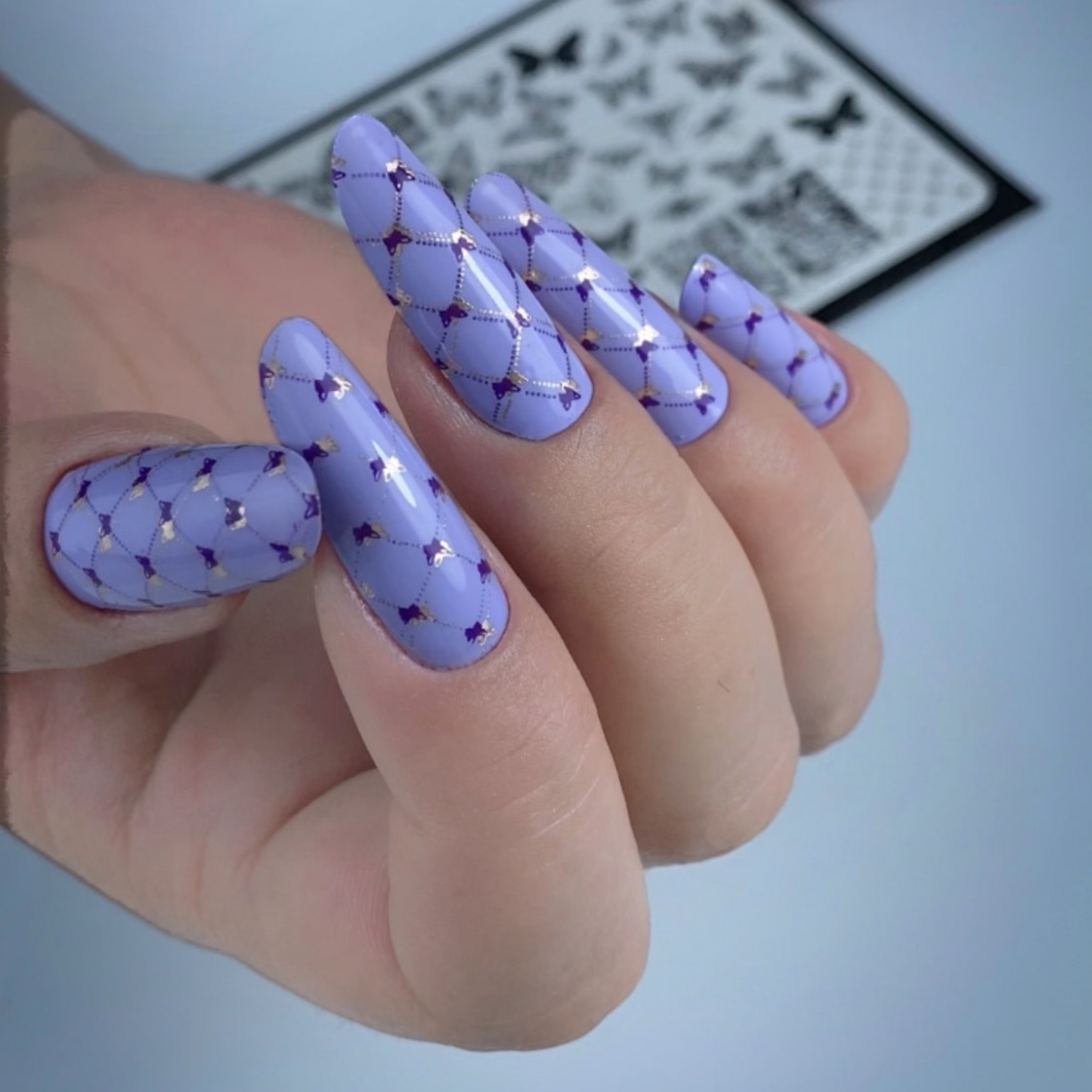 Hand with purple nail art and nail polish bottles in the background