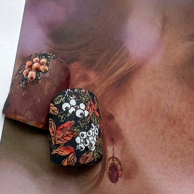 Nail tips with design of berries on tree branch on top of a magazine page