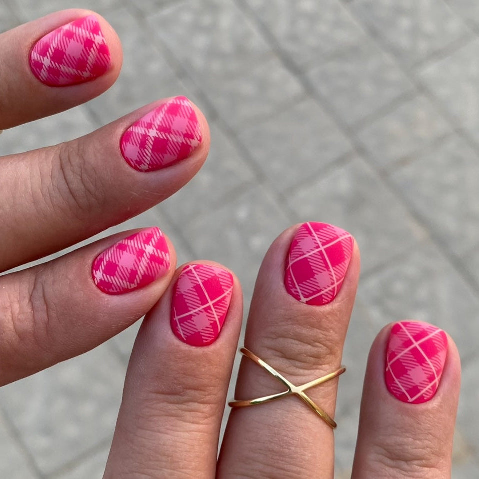 Hand with pink plaid nail design on a gray pavement background