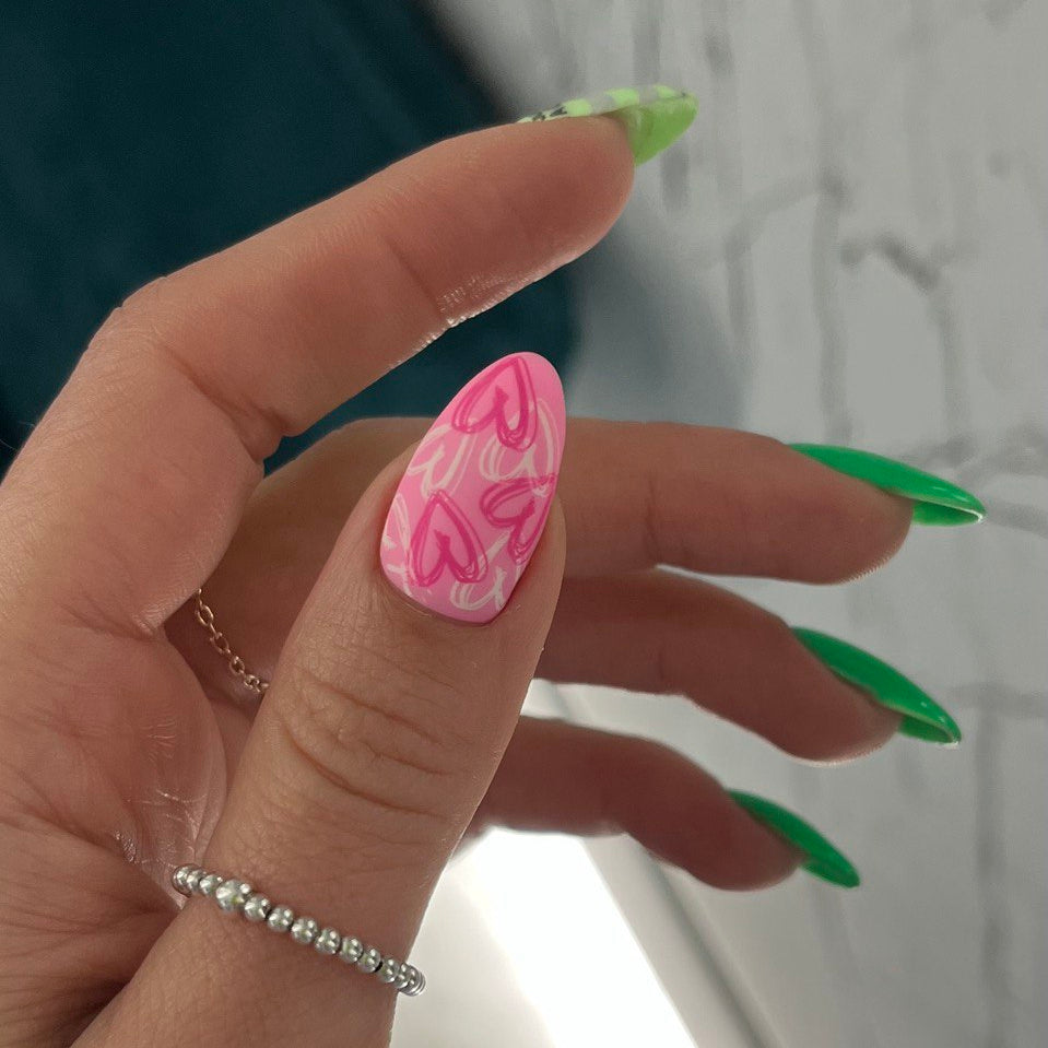 Hand with green and pink nail polish holding a small object against a neutral background