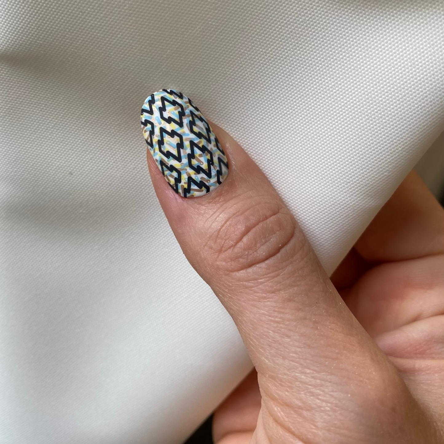 Close-up of a hand with a patterned nail on a white fabric background