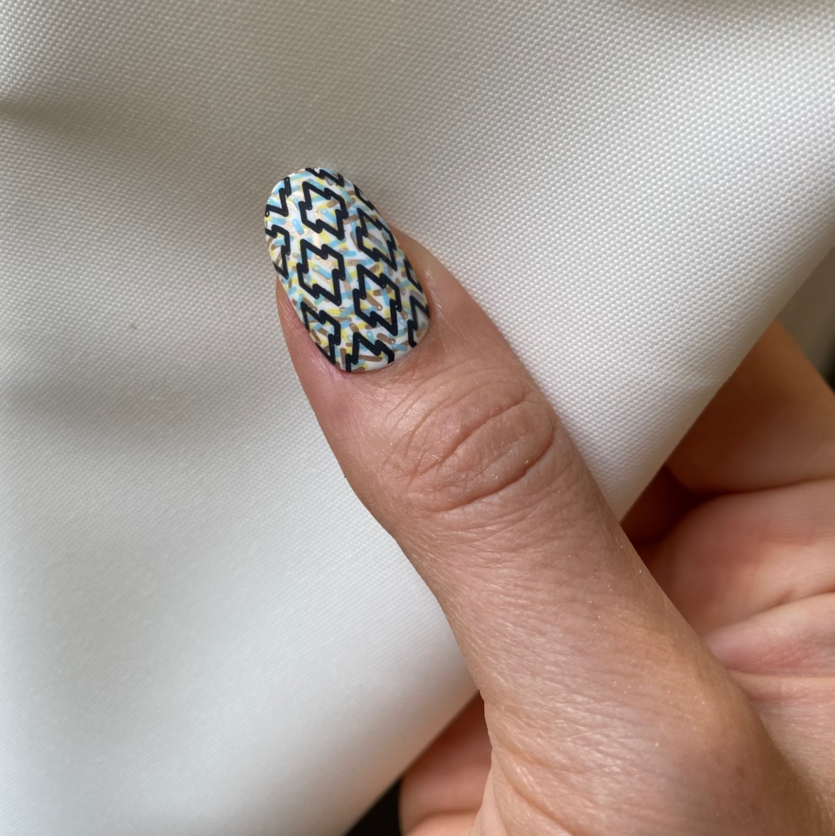 Close-up of a hand with a patterned nail on a white fabric background
