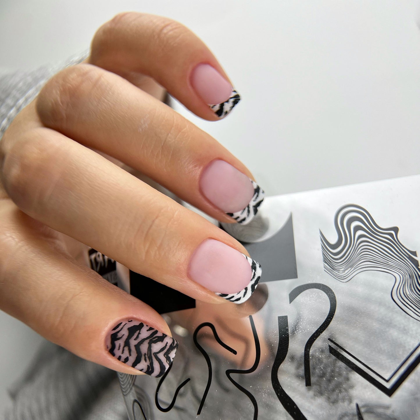 Hand with pink nails and black and white patterned design holding a gray card with black designs.