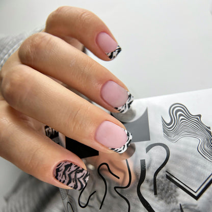 Hand with pink nails and black and white patterned design holding a gray card with black designs.