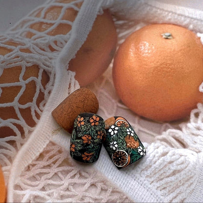 Decorative earrings with floral patterns on a white textured surface with oranges.