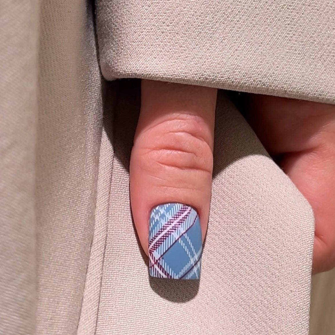Nail with blue and pink plaid design on a beige fabric background