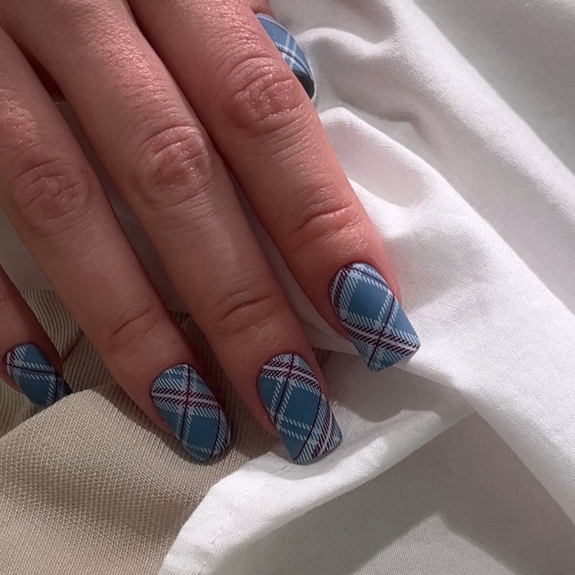 Close-up of hand with blue plaid nail design on a white fabric background