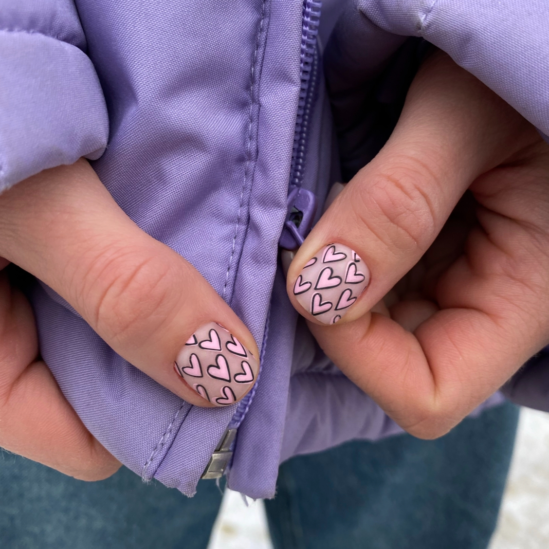 Close-up of hands with heart-patterned nails on a purple jacket background
