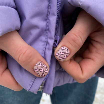 Close-up of hands with heart-patterned nails on a purple jacket background