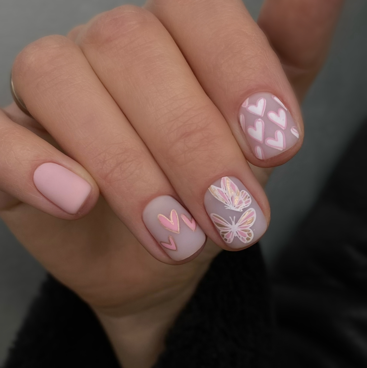 Close-up of a hand with pink heart and butterfly nail designs on a neutral background