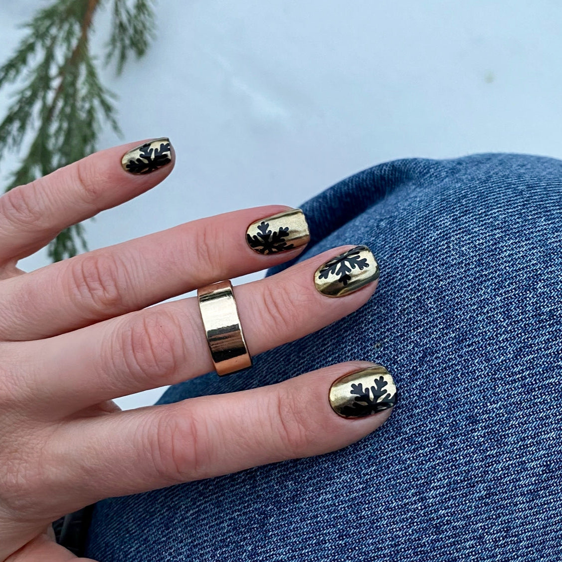 Hand with gold nail polish and ring against a blue denim background
