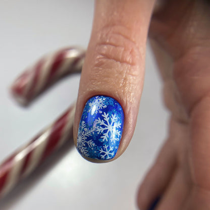 Nail with blue nail polish and snowflake design held by a hand.