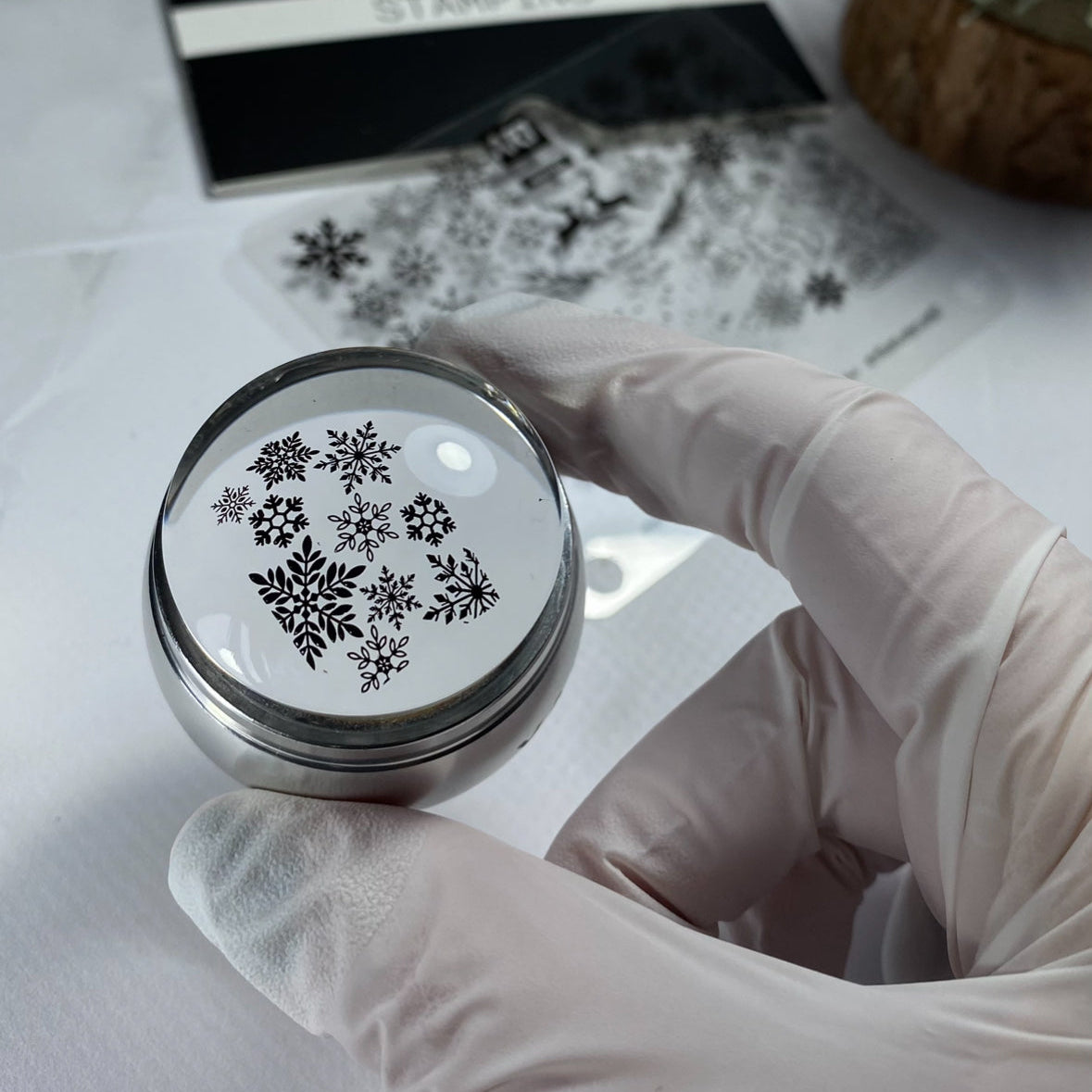 Hand holding a round stamp with snowflake designs on a white surface.