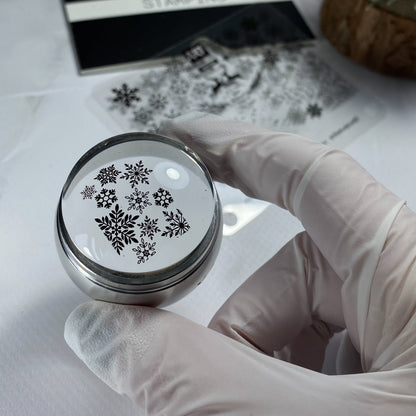Hand holding a round stamp with snowflake designs on a white surface.
