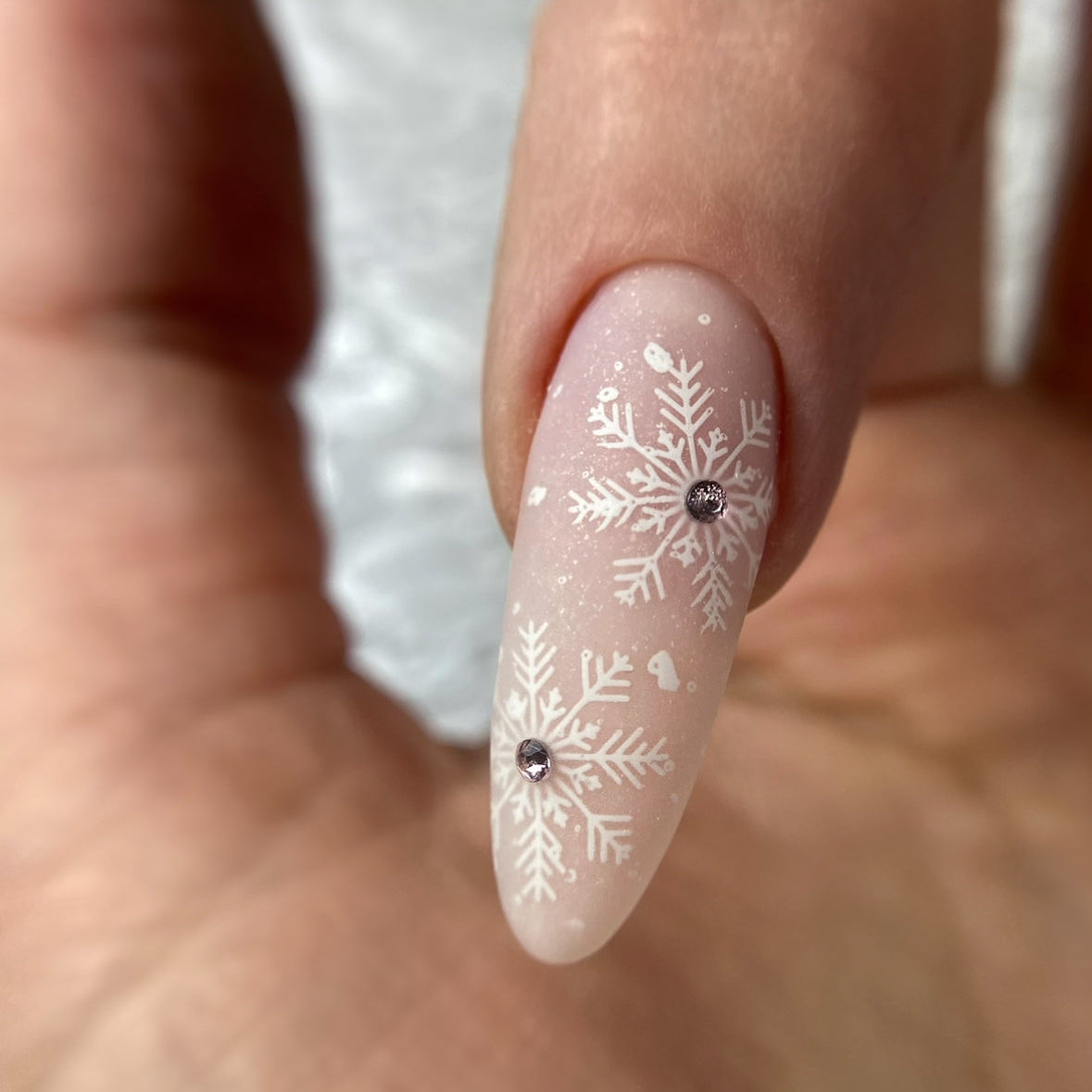 Nail with white snowflake design and rhinestone on a light background