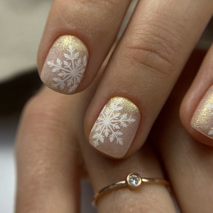 Nails with gold and white snowflake design on a neutral background