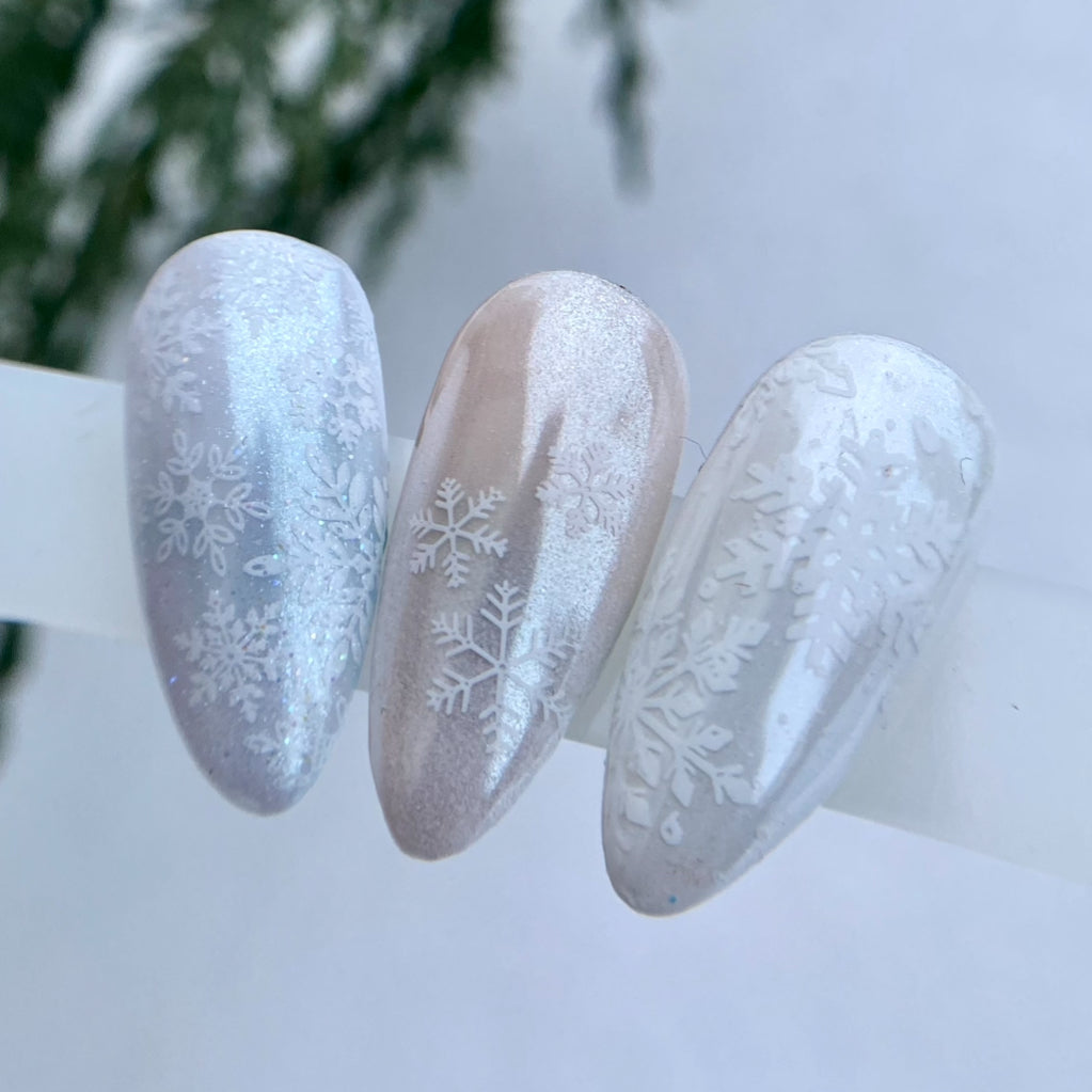 Three nails with snowflake designs on a blurred snowy background
