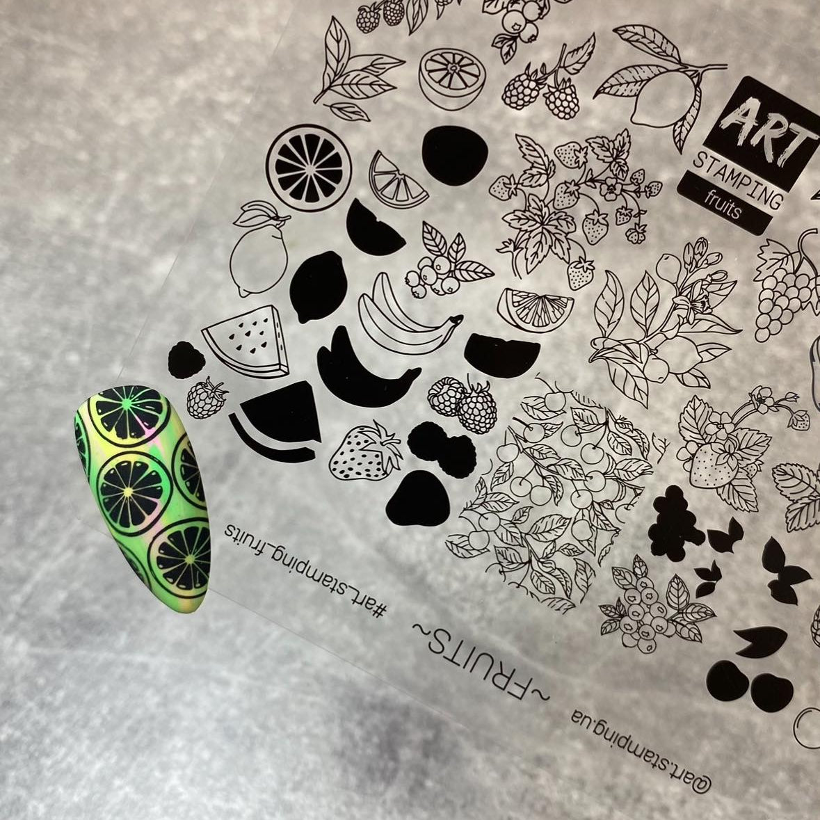 Fruit-themed nail art stamping plates on a textured surface with a green and black nail design.