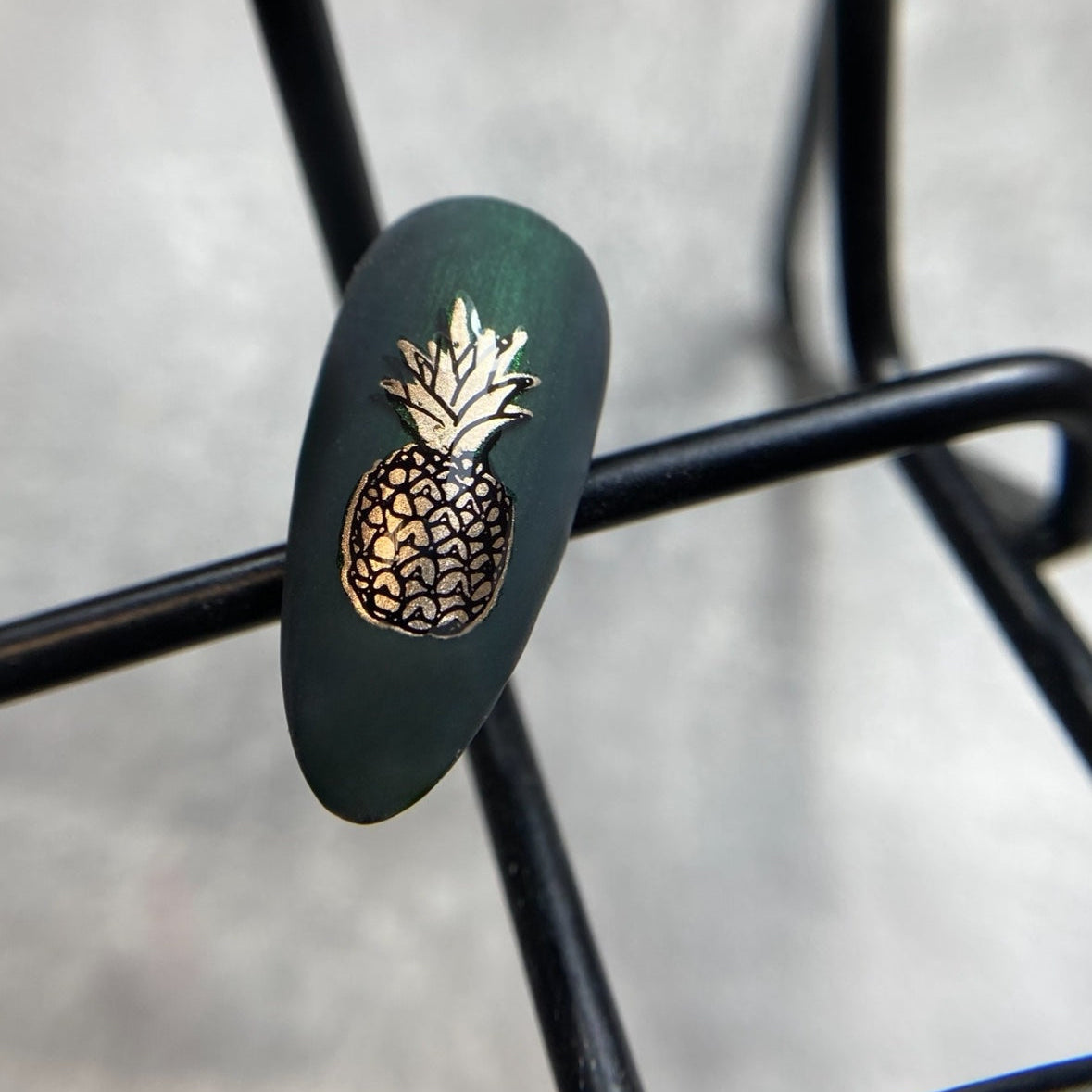 Nail with green polish and gold pineapple design on nail tips
