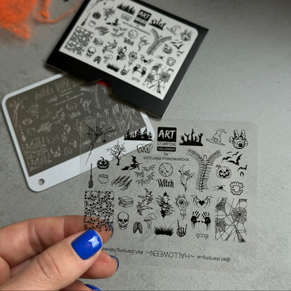 Set of Halloween-themed stamping plates on a gray surface with a hand holding one plate.