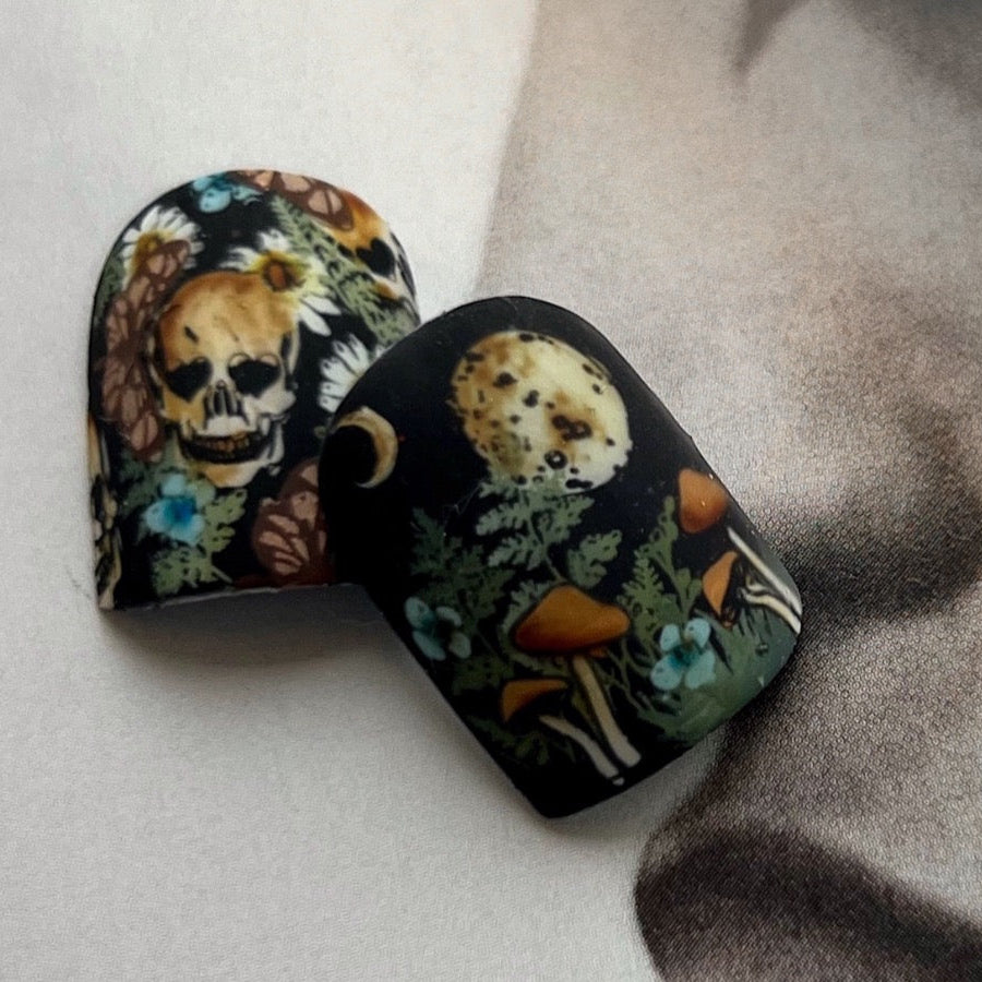 Nail tips with skull and nature designs on a textured surface.