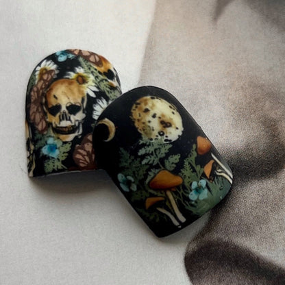 Nail tips with skull and nature designs on a textured surface.