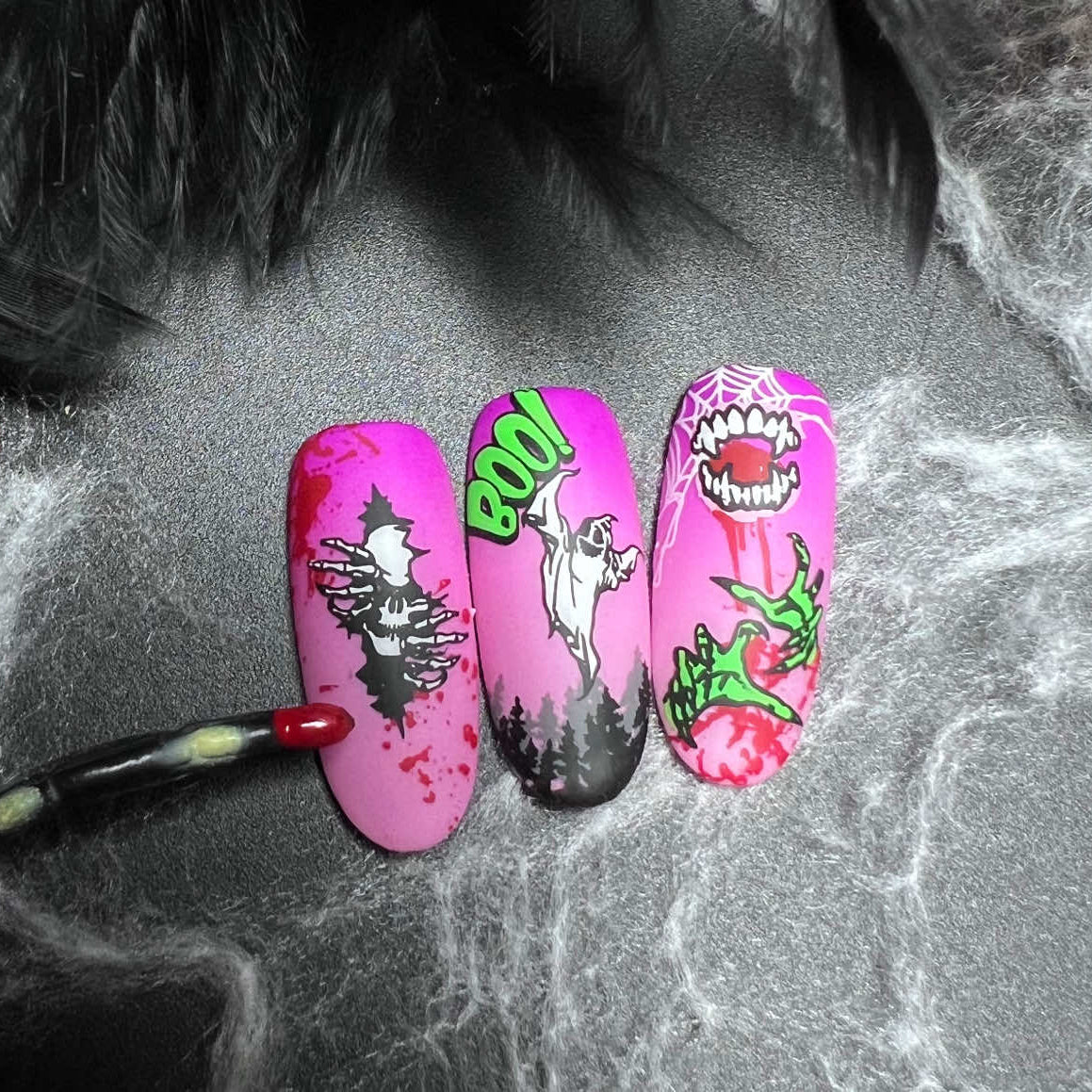 Three pink nail art designs on a textured surface with a brush.