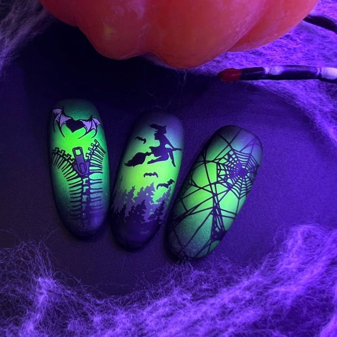 Halloween-themed nail art with glowing designs on a dark background