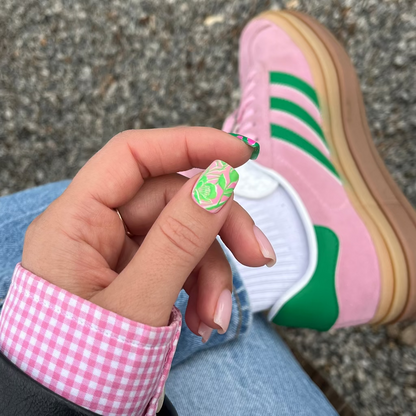 Person wearing pink Adidas shoes with green stripes, sitting on a concrete surface.