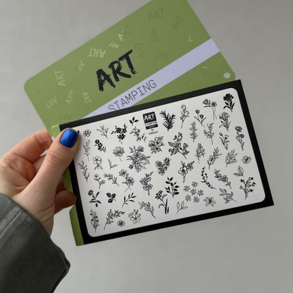 Hand holding a stamping plate with floral designs on a gray background