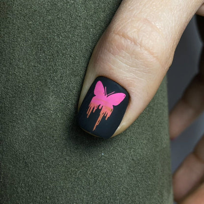 Nail with black polish and pink butterfly design on a green surface