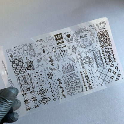 Sheet of black designs on clear plastic held by a gloved hand against a light gray background